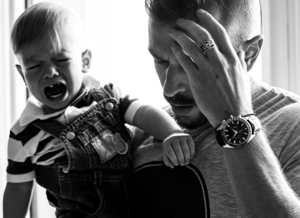 Overtired toddler crying while exhausted parent provides comfort and support