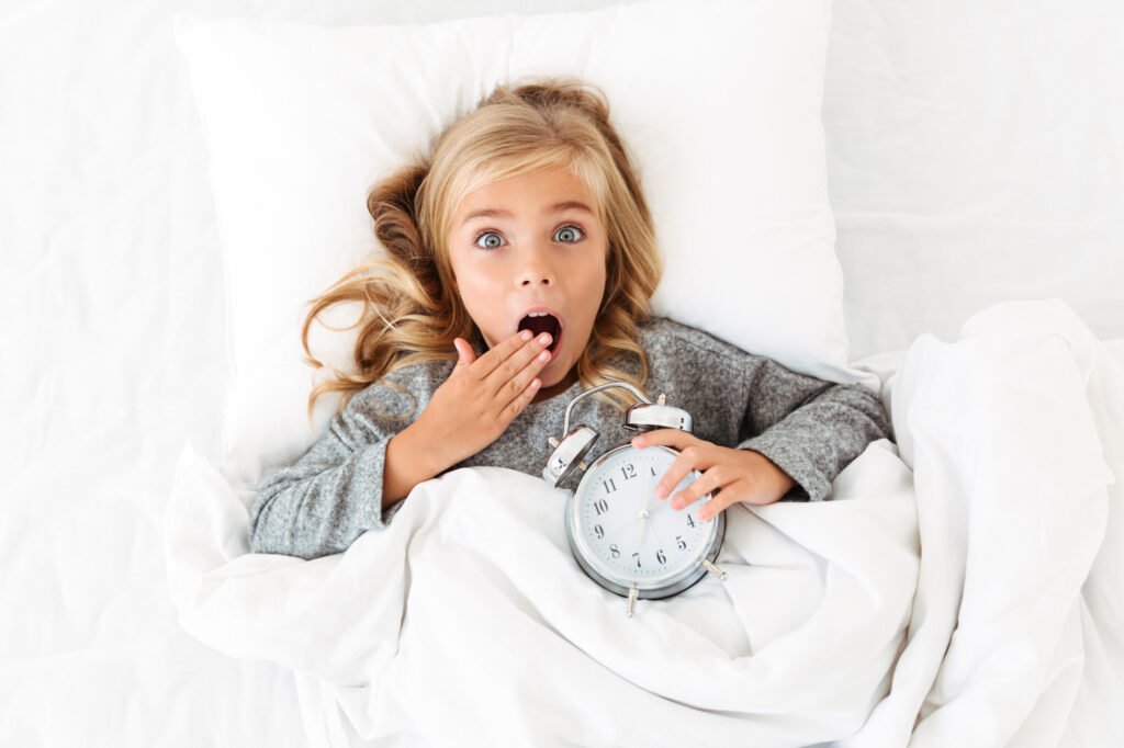 Child wakes at 5am in bed holding an alarm clock