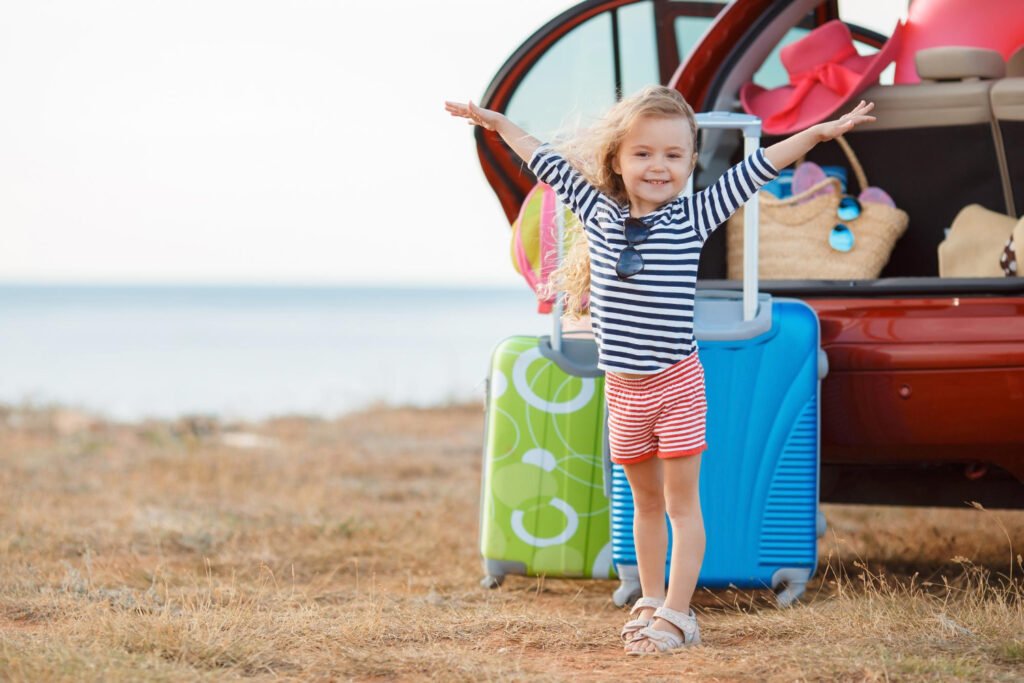 Travelling with Children and Sleep, girl standing beside holiday luggage and a family car, ready for travel while maintaining healthy sleep routines on holiday.
