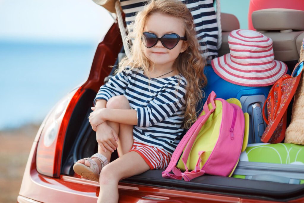Young girl sitting in the boot of a car with holiday luggage, representing family traveling with children and sleep on holiday