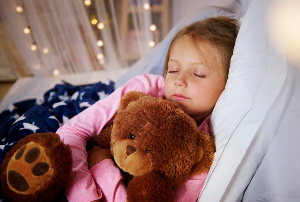 Young child sleeping peacefully with a teddy bear during a daytime nap, supporting healthy sleep development.